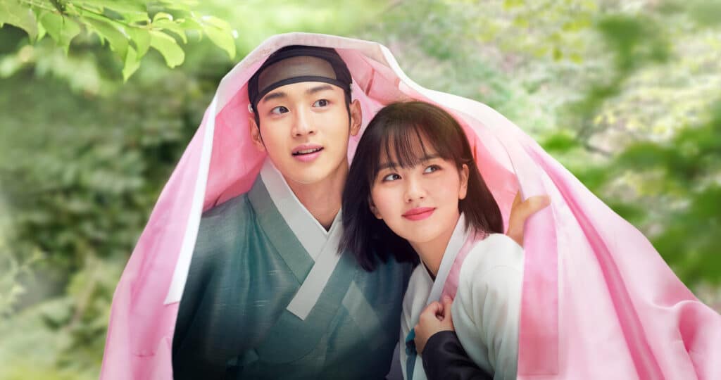 Jang Dong-yoon disfarçado de mulher e Kim So-hyun, personagens principais do dorama "O Conto de Nokdu", escondidos sob um lenço cor-de-rosa.