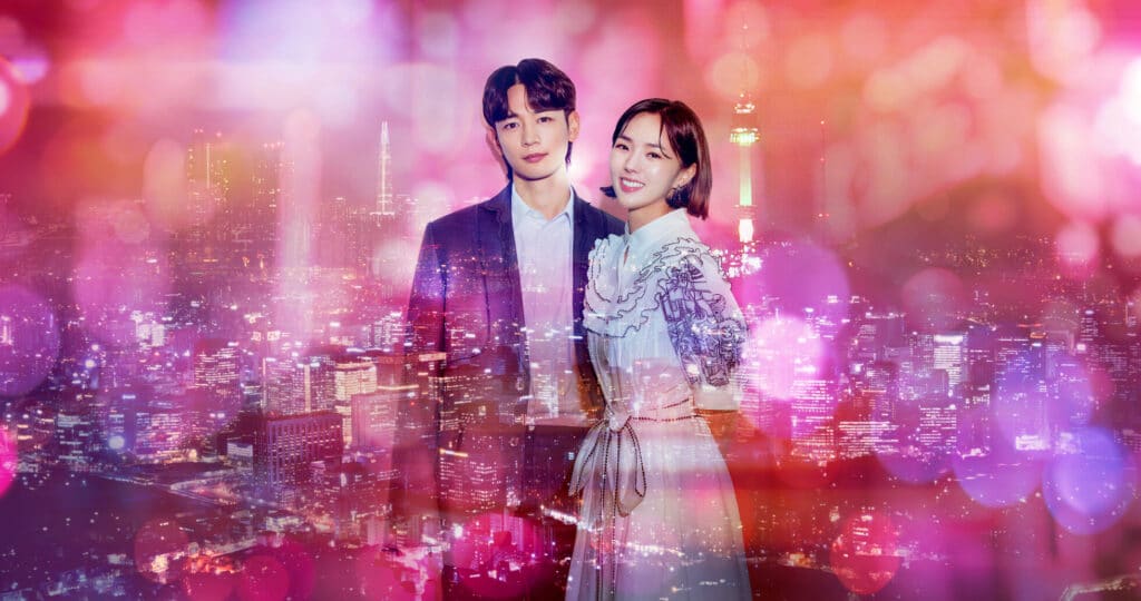 Os atores Chae Soo-bin e Choi Min-ho, protagonistas do dorama ‘The Fabulous’, sorriem em frente a um cenário da cidade de Seul à noite, destacando o universo da moda coreana.