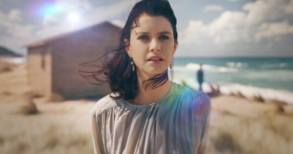 Atiye, a protagonista da série O Segredo do Templo, olhando diretamente para a câmera em uma praia na Turquia.