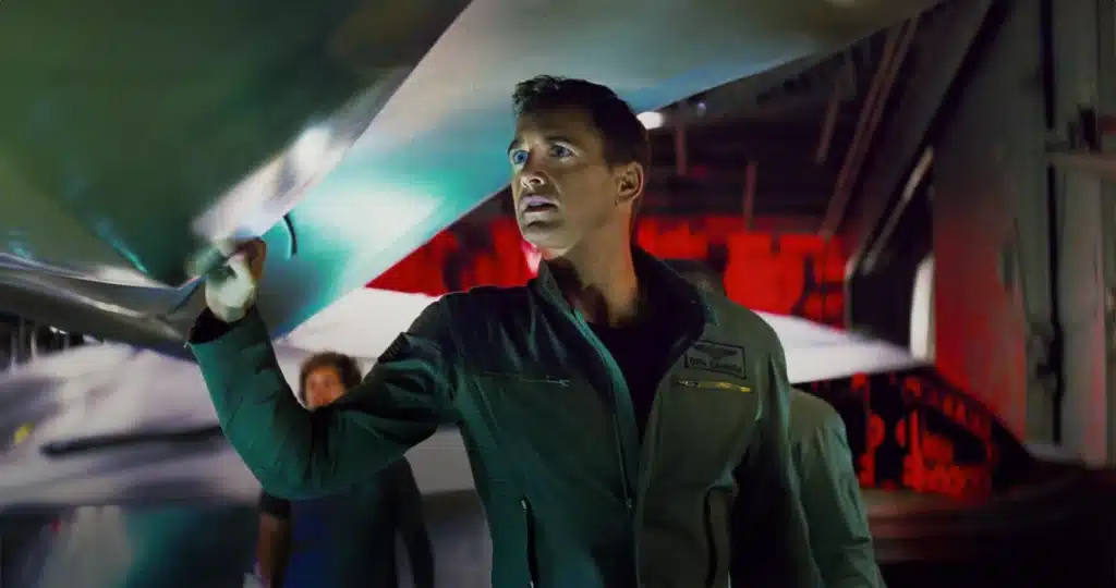 Piloto no hangar diante de jato de combate, com expressão preocupada após falha do sistema