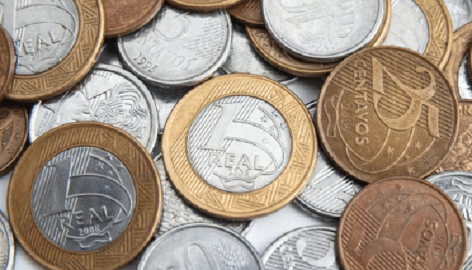 Moedas brasileiras de 1 real e centavos em diferentes anos agrupadas sobre uma superfície branca.