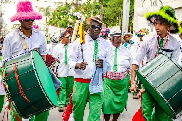 Grupo de músicos e dançarinos participando da Congada de Minas Gerais, vestindo trajes tradicionais e coloridos, com chapéus e instrumentos musicais.