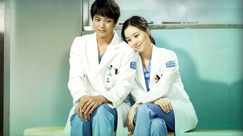 Os protagonistas da série 'Good Doctor', Cha Yoon-seo e Park Si-on, ambos com jalecos brancos, estão sentados lado a lado, enquanto ela repousa a cabeça no ombro dele.