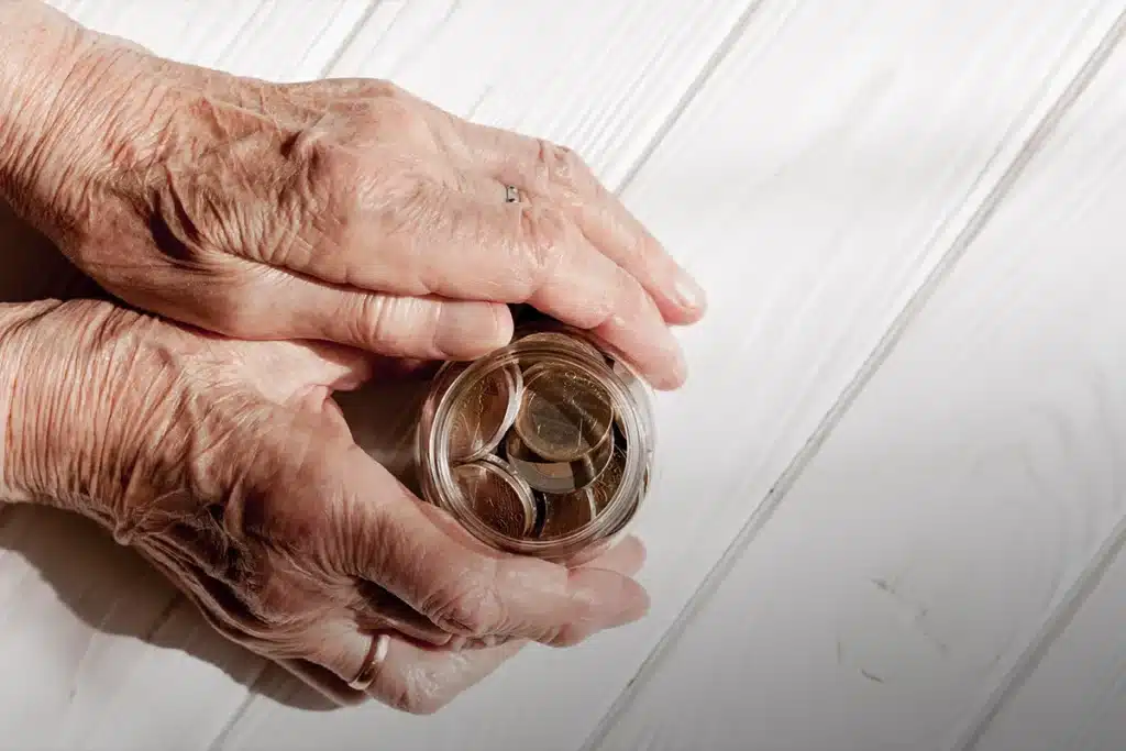Mãos de idoso segurando um pote com moedas, simbolizando o acúmulo de benefícios como aposentadoria e pensão por morte.