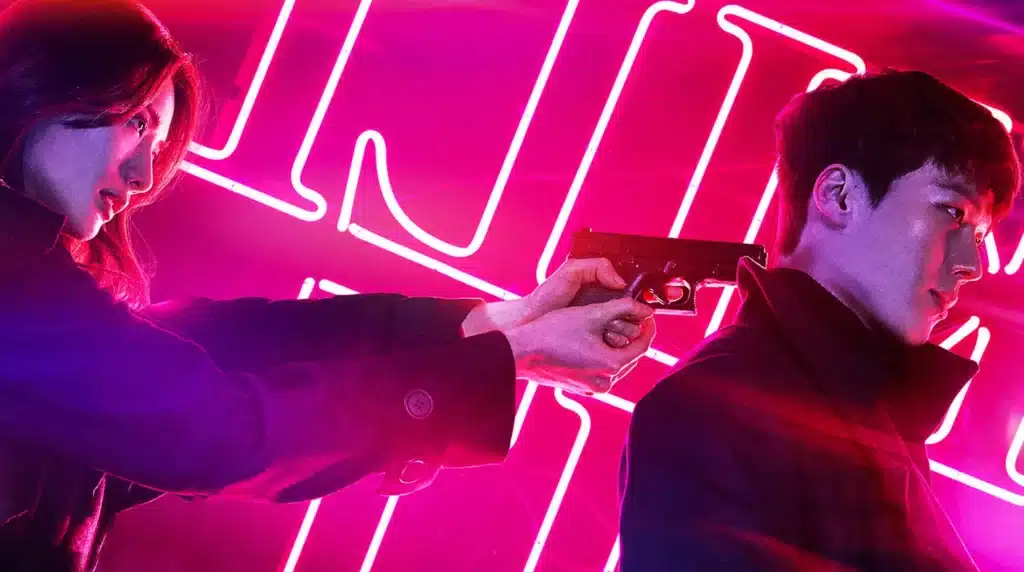 Cena de ação do dorama Kill It, com mulher segurando uma arma atrás de um homem, ambos com expressão intensa.