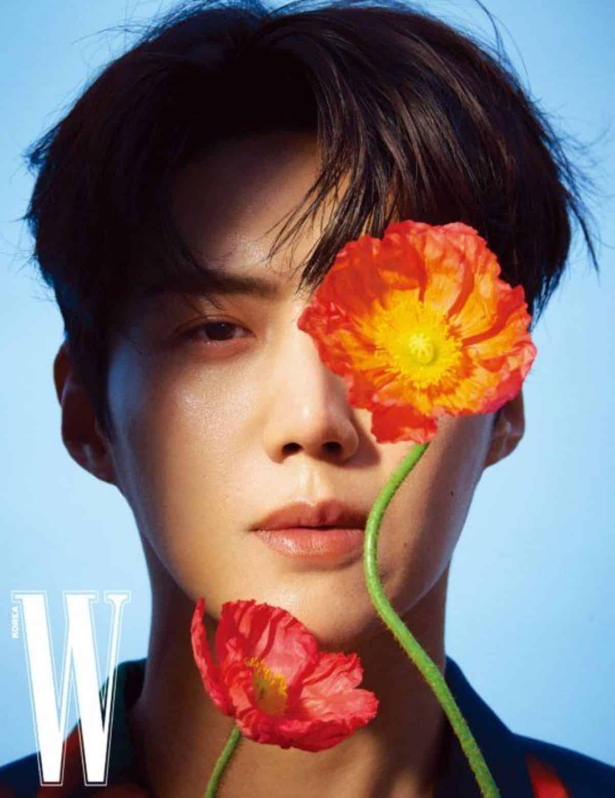 O ator coreano Kim Seon-ho em uma foto de capa de revista, com duas flores vermelhas cobrindo parte de seu rosto.
