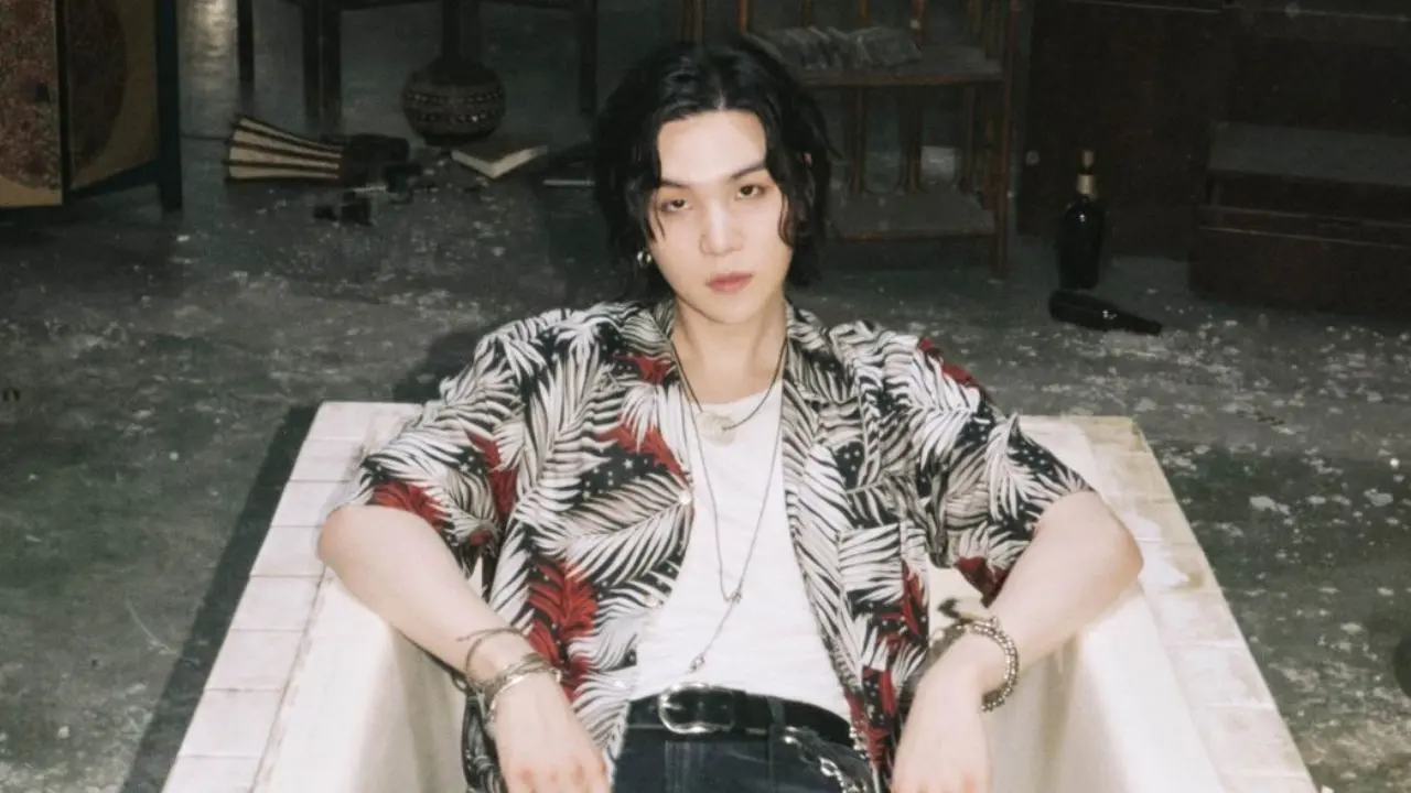 Suga do BTS, em estilo casual, relaxando em um cenário artístico