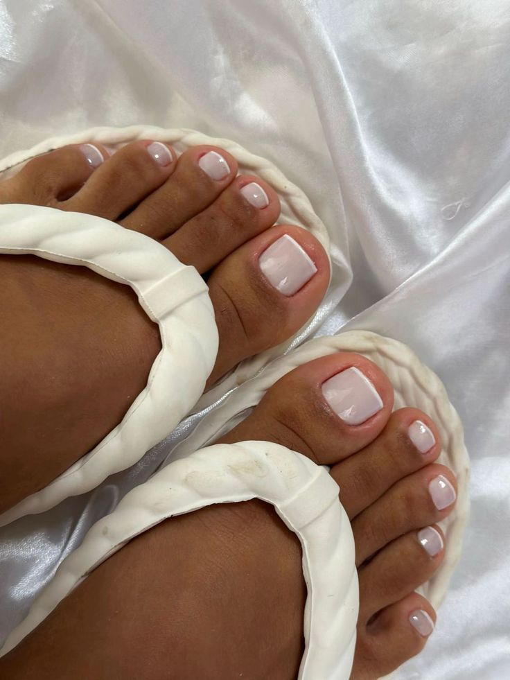 Pedicure estilo francesinha branca e elegante nas unhas dos pés, demonstrando uma cor que alonga e embeleza visualmente o formato das unhas.