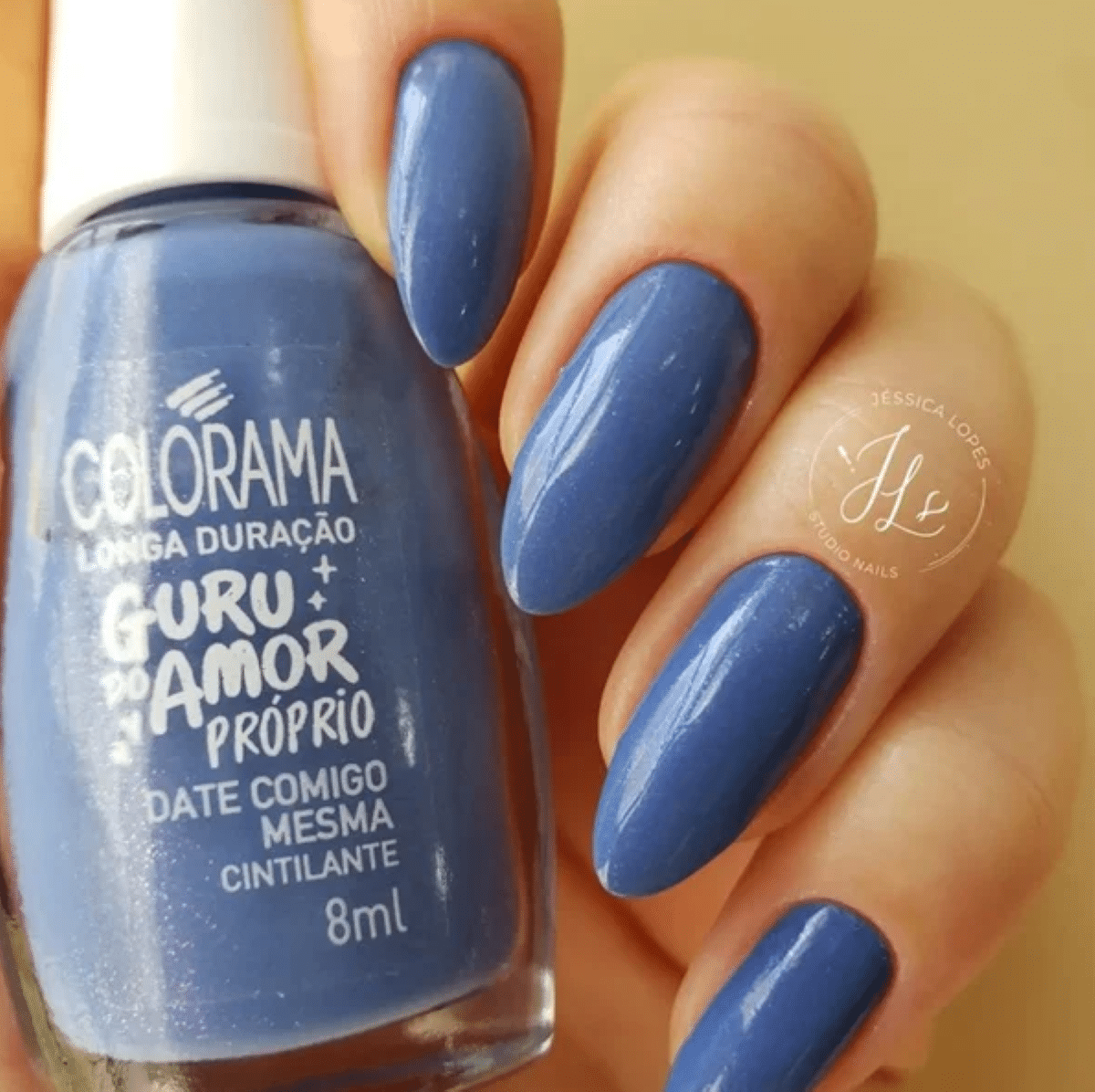 Mãos com unhas pintadas de esmalte azul-acinzentado (cerúleo) e frasco de esmalte Colorama ao lado.