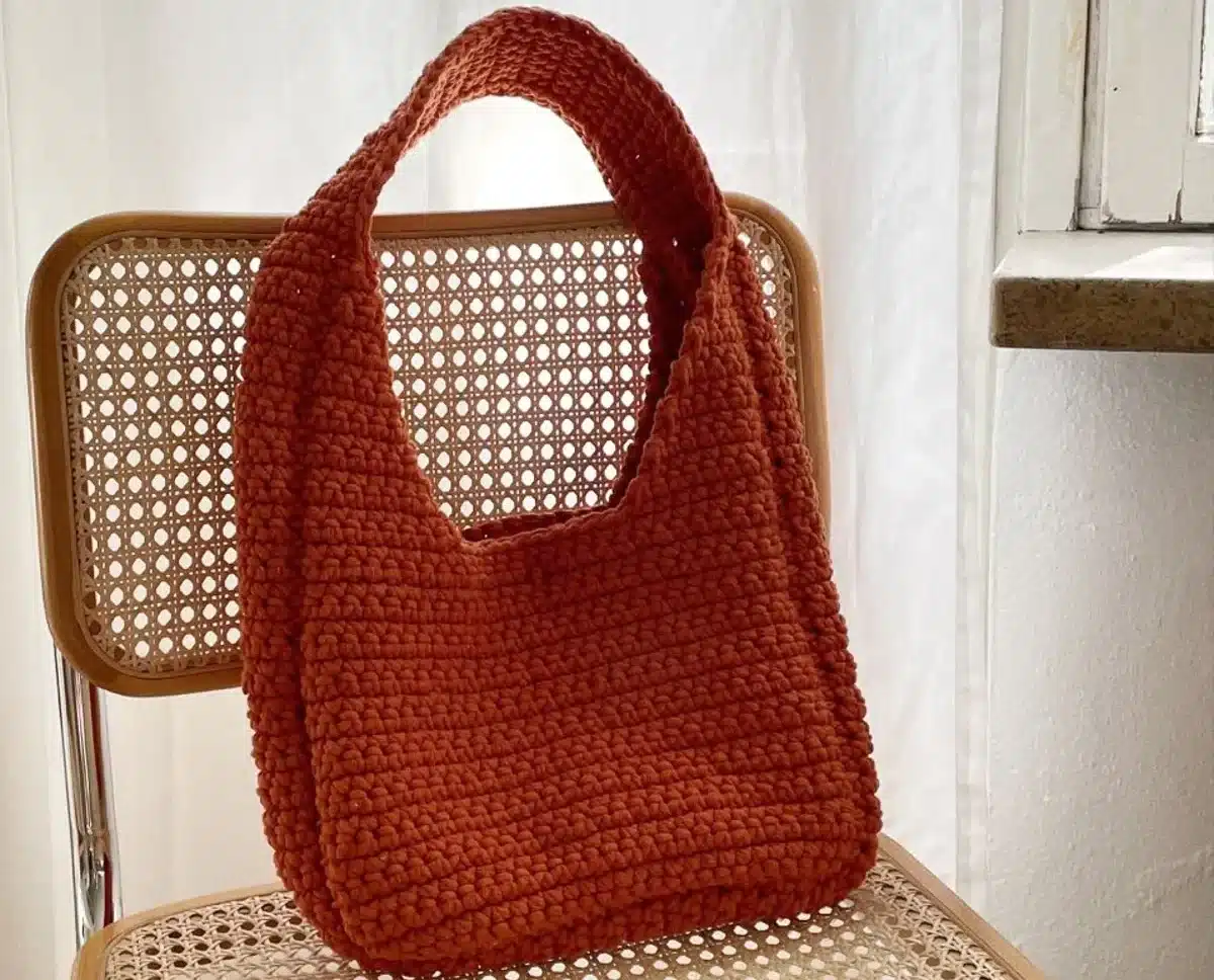 Bolsa de crochê laranja feita à mão sobre uma cadeira de vime, em ambiente iluminado