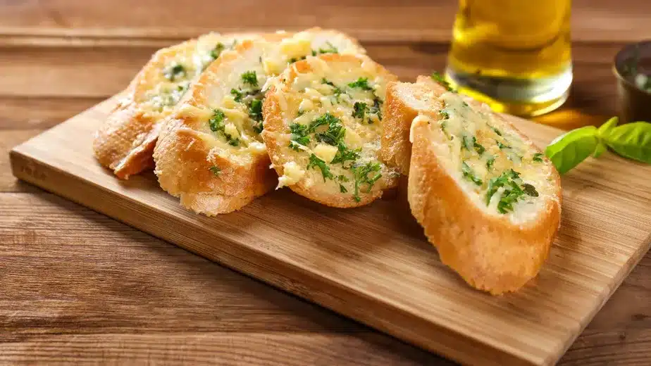 Pão de alho recheado com queijo e ervas sobre uma tábua de madeira.