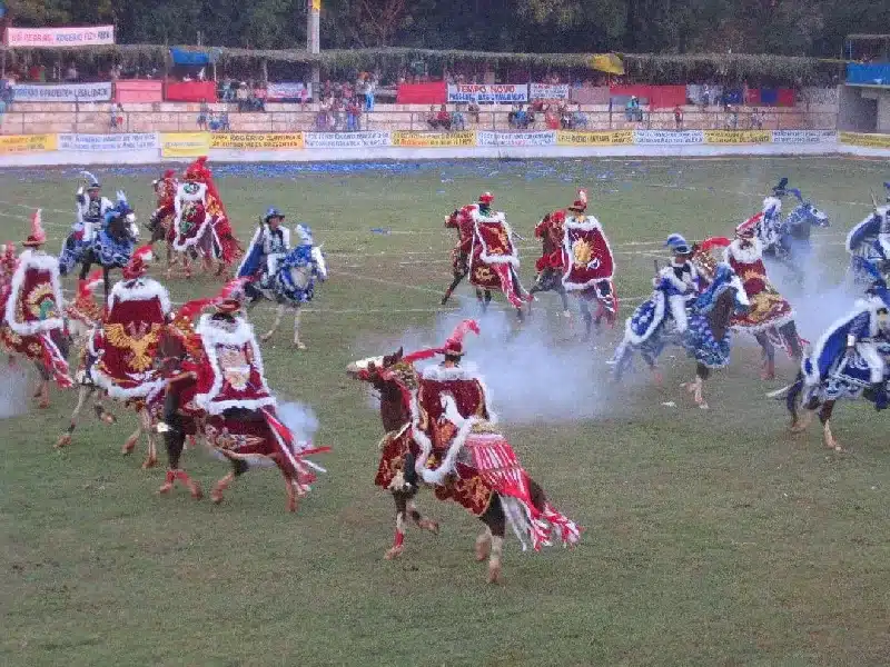 Grupo de cavaleiros montados em cavalos, vestindo trajes tradicionais coloridos e participando da batalha teatral da Cavalhada de Pirenópolis durante a Festa do Divino Espírito Santo.