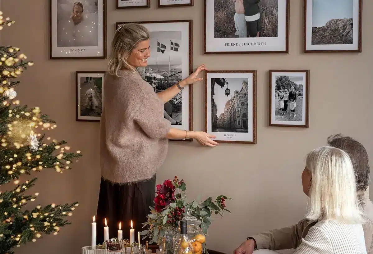 Pessoa ajustando quadros decorativos na parede com uma árvore de Natal ao fundo em uma sala de estar aconchegante.