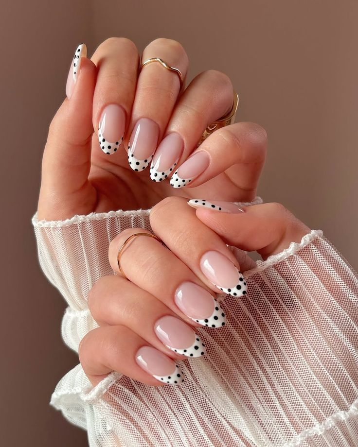 Mãos com unhas decoradas em estilo francesinha, com as pontas brancas adornadas por bolinhas pretas (poá).