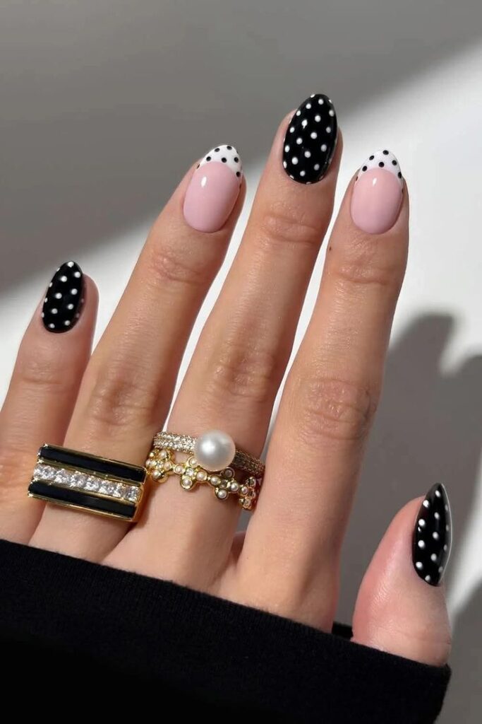 Unhas em gel decoradas com poá preto e branco em fundo nude, com um anel prateado no dedo anelar.