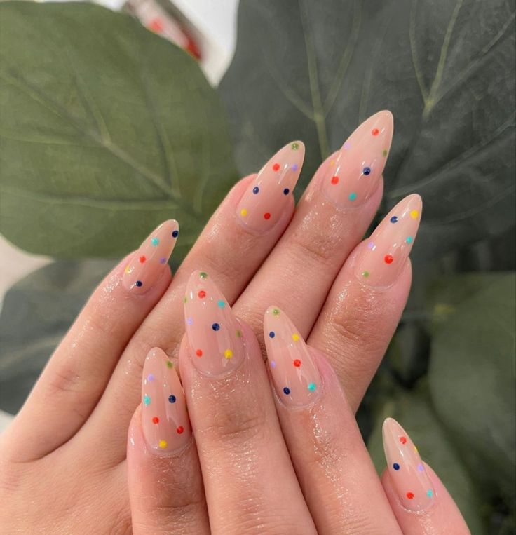 Unhas em gel transparentes com bolinhas de poá coloridas em tons de rosa, azul e amarelo, com um anel delicado.