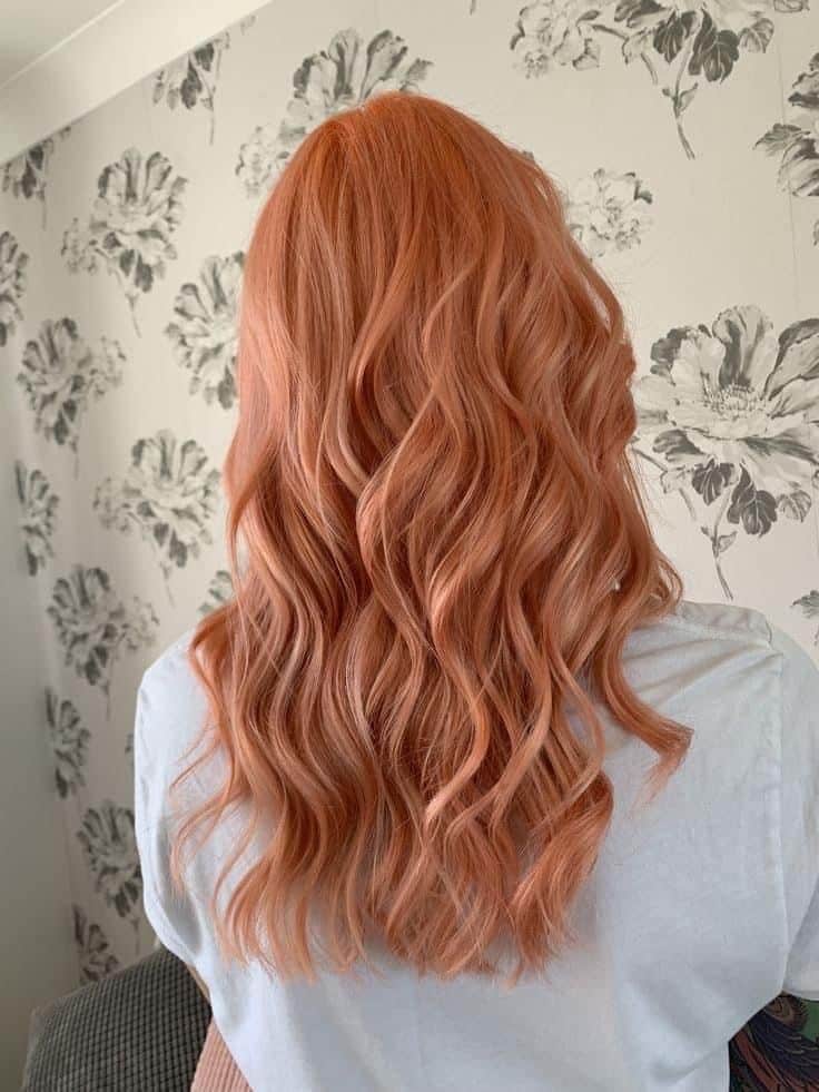 Cabelo médio ondulado com coloração em tom de pêssego, uma das cores vibrantes em alta para a primavera.