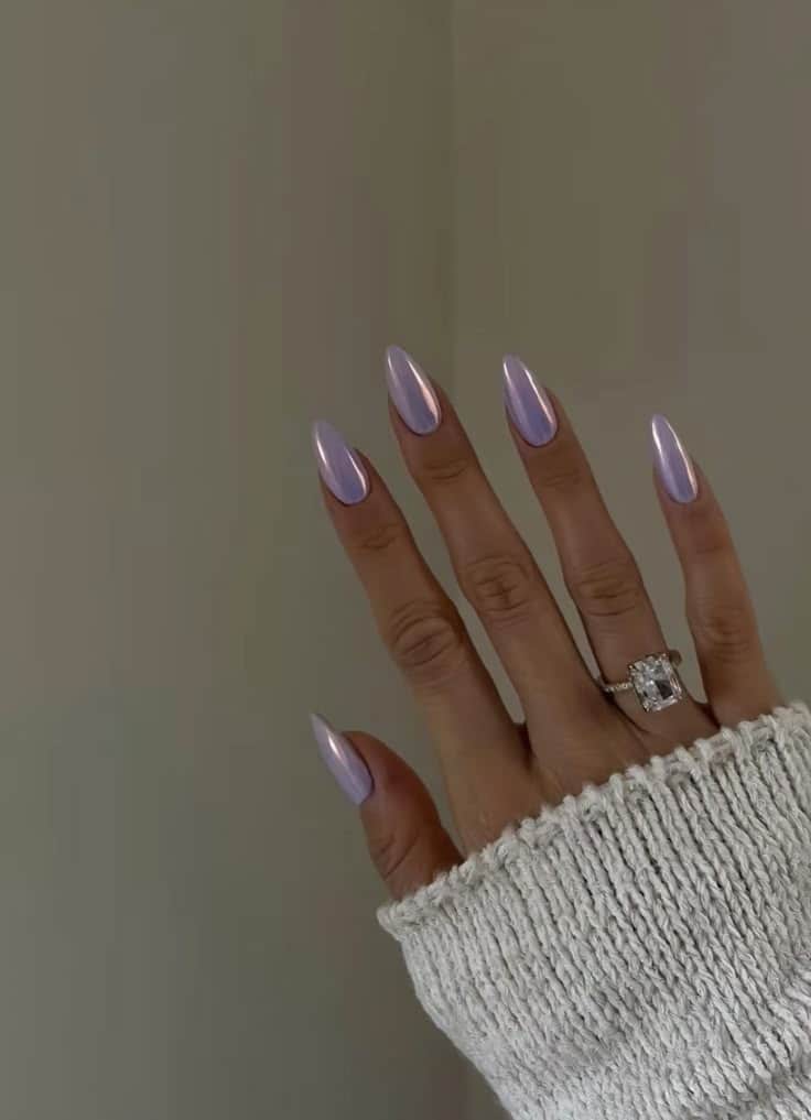 Unhas longas e amendoadas com esmalte em tom lilás leitoso e acabamento cintilante, representando a tendência de unhas minimalistas e elegantes.