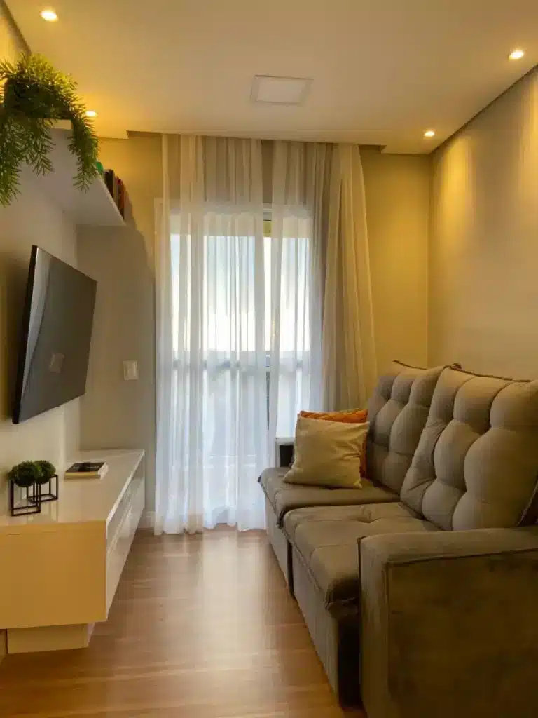 Imagem de um ambiente moderno com sofá, TV e cortinas leves, destacando a iluminação suave no teto.