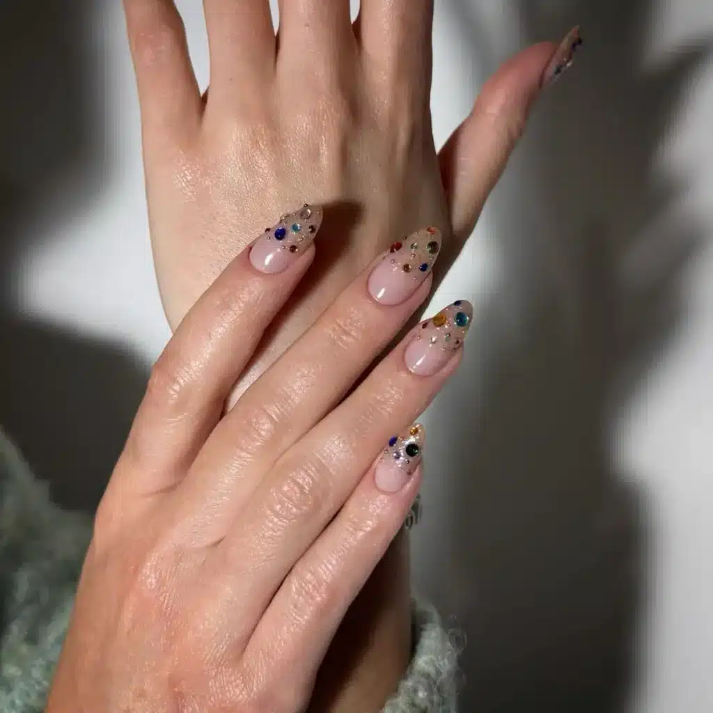 Unhas decoradas com pedrarias coloridas e brilho.