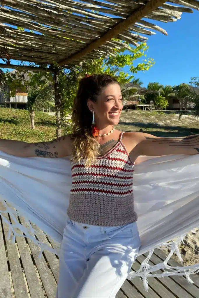 Mulher sorrindo ao ar livre usando uma regata de crochê com alças finas.