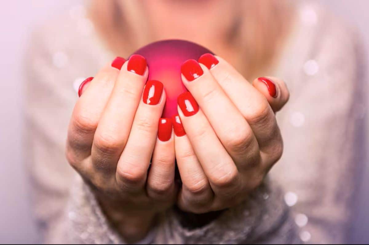 Mãos de uma mulher segurando uma esfera vermelha com unhas pintadas de esmalte vermelho vivo.