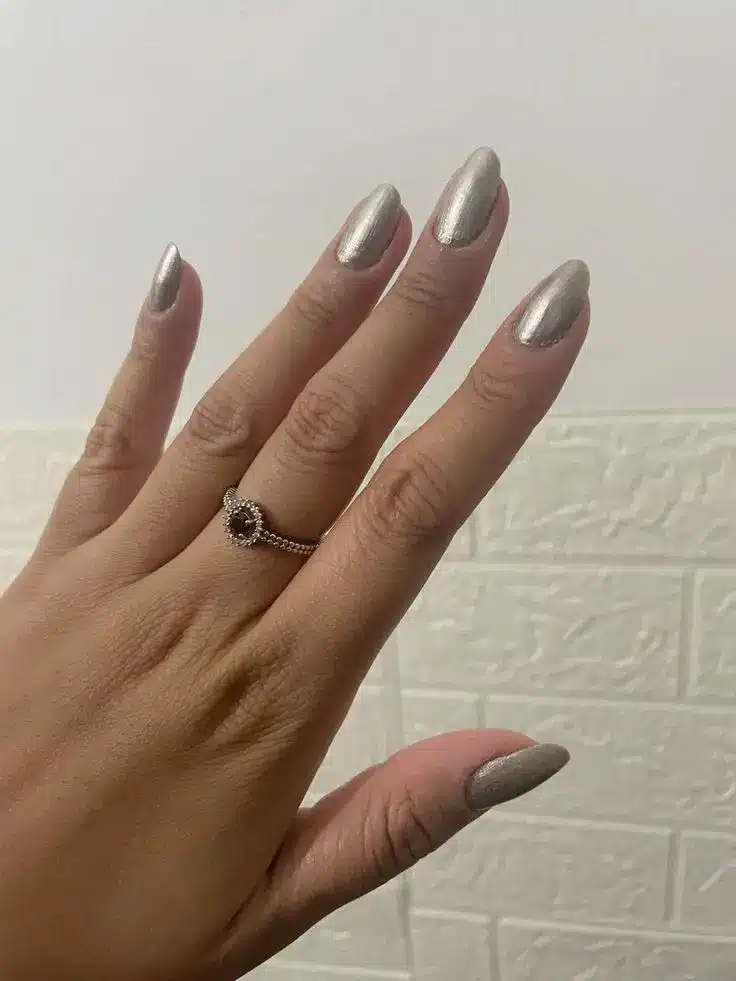 Mão feminina com unhas esmaltadas em tom metálico, efeito aço escovado.