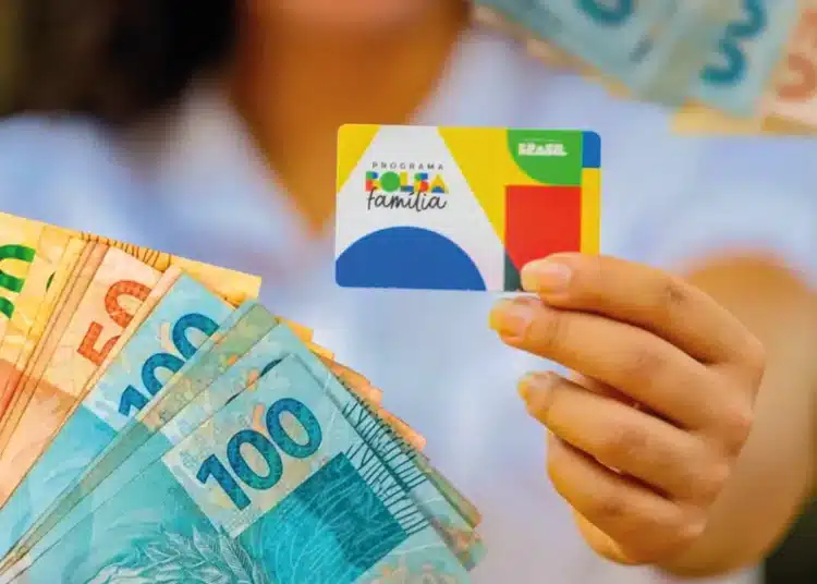 Imagem ilustrativa do Bolsa Família mostrando uma mão segurando o cartão do programa junto a notas de reais de diferentes valores, com destaque para as cédulas de 100, 50 e 20 reais.