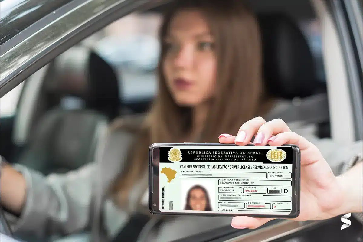 Pessoa mostrando sua CNH digital no celular enquanto está dentro de um carro, ilustrando a digitalização do processo de habilitação no Brasil.