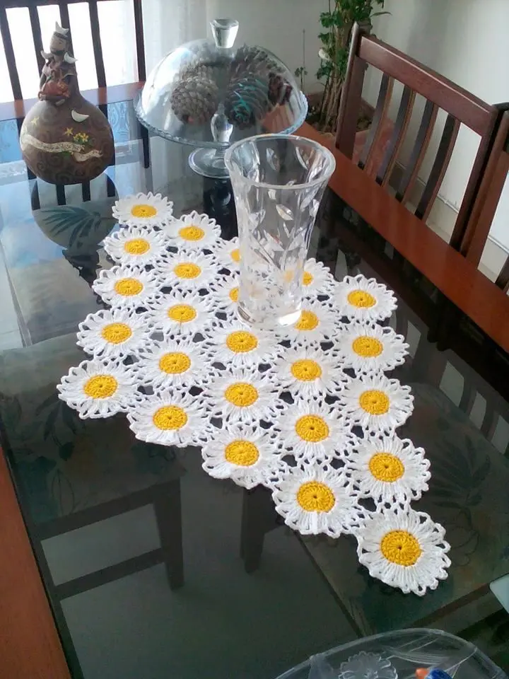 Caminho de mesa em crochê com flores de margarida amarelas e brancas.