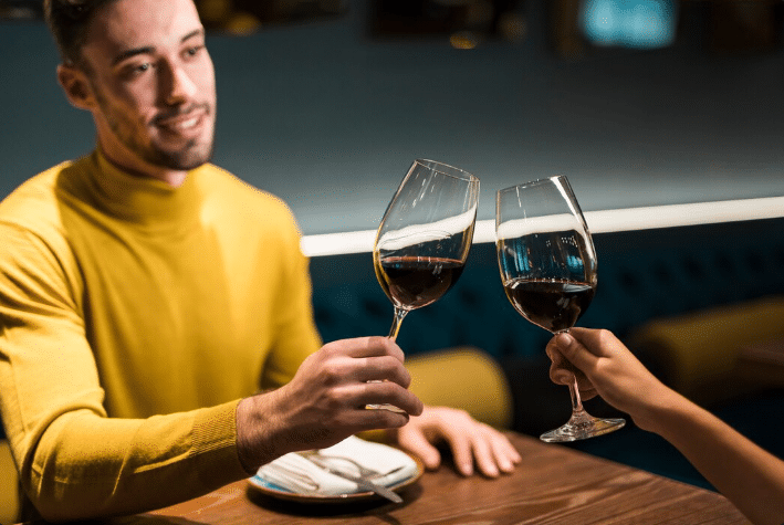 Casal fazendo um brinde com taças de vinho tinto em restaurante, celebrando o consumo seguro de bebidas fermentadas.