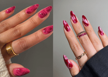 Duas mãos com unhas stiletto alongadas em tons de rosa e vermelho, apresentando a nail art em efeito mármore e rosas.