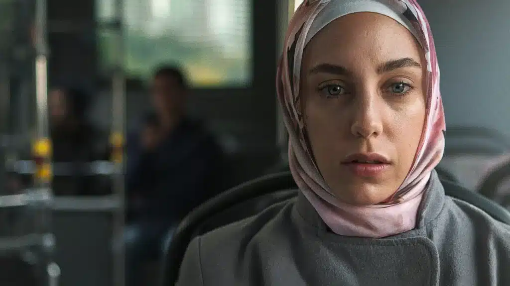 Imagem da personagem com hijab, sentada em um transporte público, refletindo sobre a trama psicológica e social de 'Ethos'.