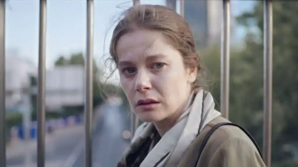 Fatma, uma mulher com expressão angustiada, presa entre as grades de um cercado enquanto reflete sobre as consequências de suas ações.