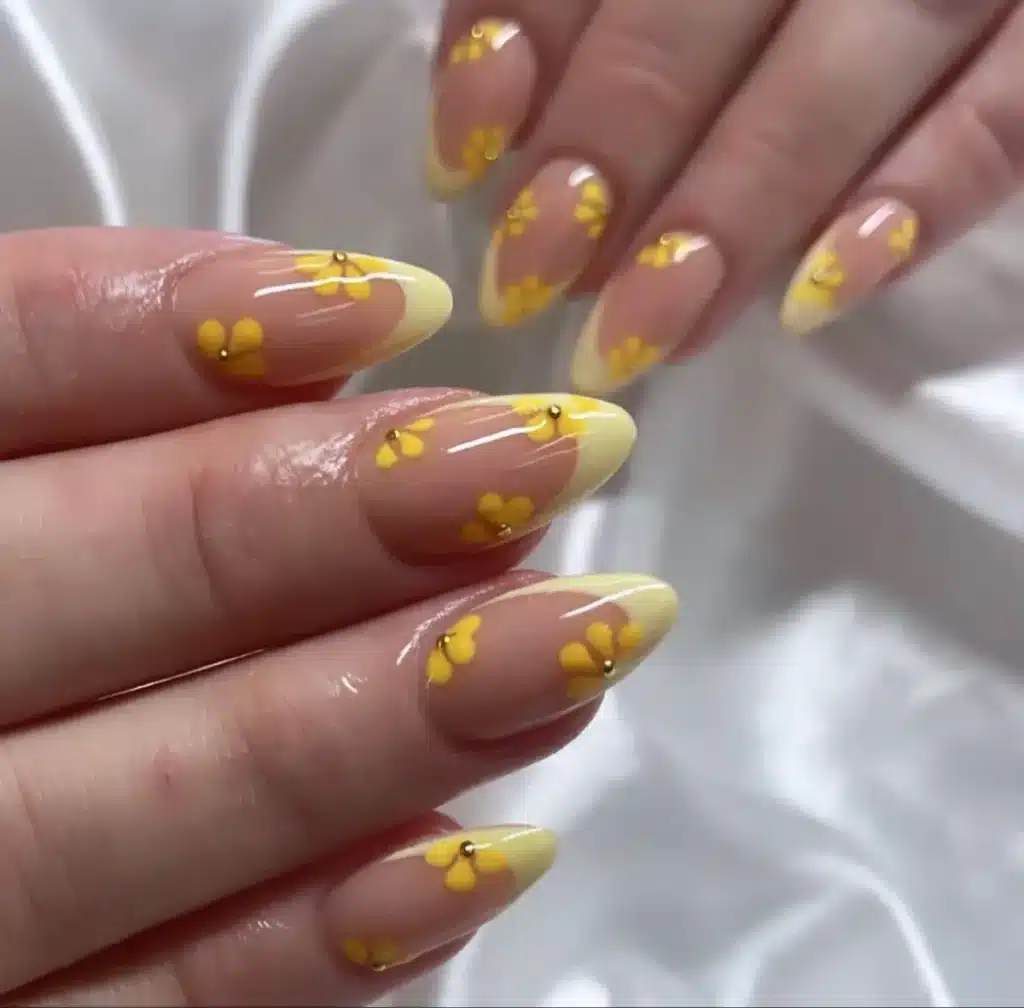 Unhas decoradas com flores amarelas delicadas e pontas em tom de amarelo claro.