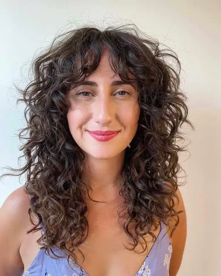 Mulher com cabelo encaracolado e franja shag, destacando um visual natural e volumoso.