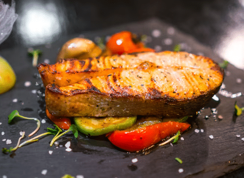 Filé de salmão grelhado acompanhado de legumes coloridos sobre prato preto