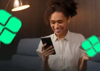Pessoa sorrindo enquanto usa o celular para realizar uma transação com cartão, representando o uso do Pix parcelado.