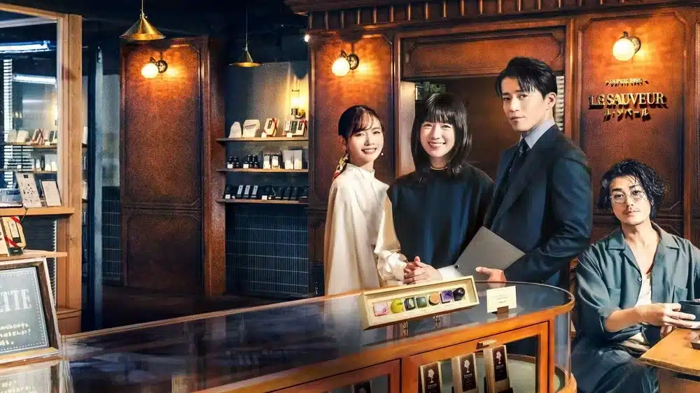 Elenco principal de ‘Românticos Anônimos’ em uma loja de chocolates elegante.