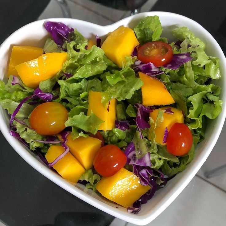 Salada tropical colorida em uma tigela de coração com alface manga em cubos e tomates cereja