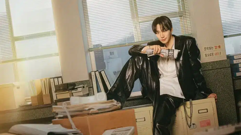 Ator de 'Typhoon Family' posando em um escritório, com uma postura confiante e roupas de couro brilhantes.