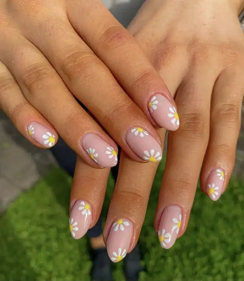 Unhas decoradas com flores de margarida em esmalte nude rosado, estilo delicado e moderno.