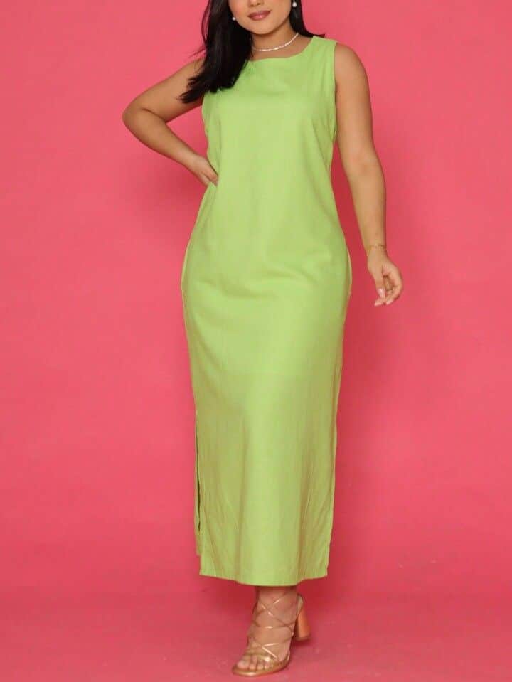 Mulher em fundo rosa usando um vestido longo reto, na cor verde lima, de linho liso e com alças largas. A modelagem estruturada e minimalista valoriza a silhueta, sendo ideal para um visual sofisticado.