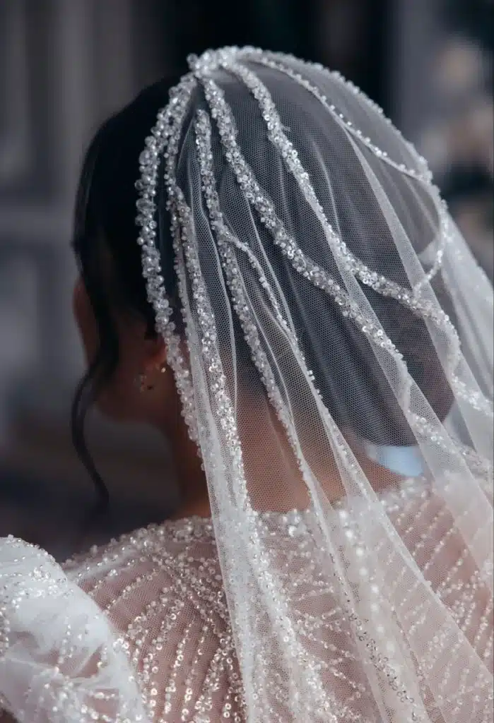 Véu de noiva com bordados e pedrarias sofisticadas, criando desenhos geométricos e realçando a renda.