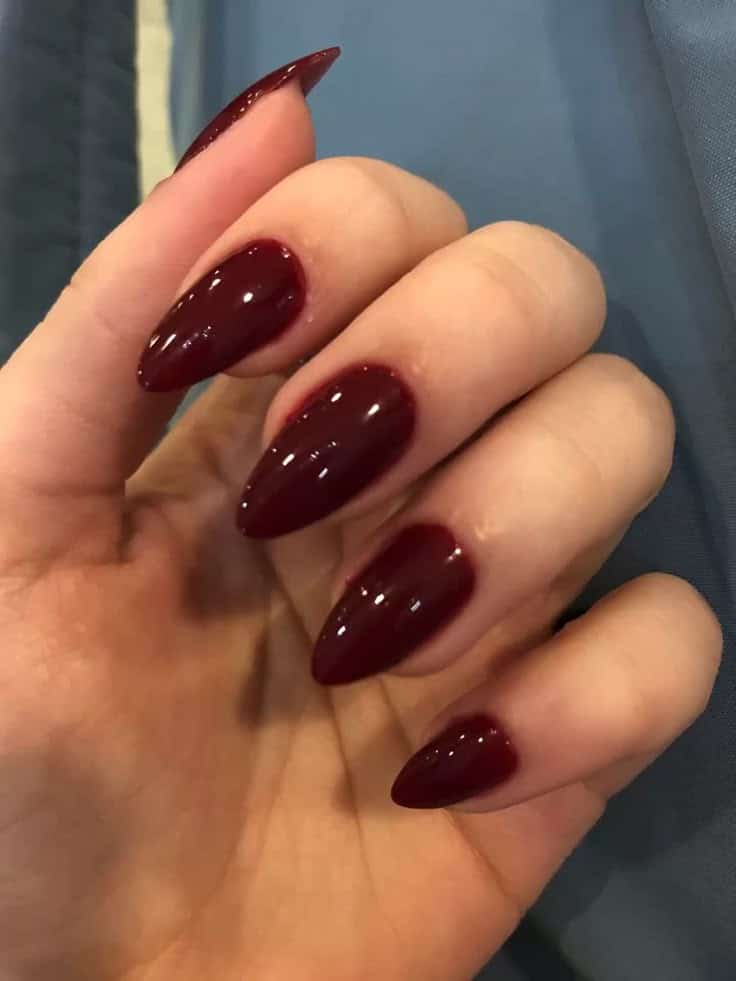 Unhas longas no formato amendoado ou stiletto esmaltadas com um tom intenso de vermelho vinho e alto brilho. A cor é uma tendência clássica e elegante.
