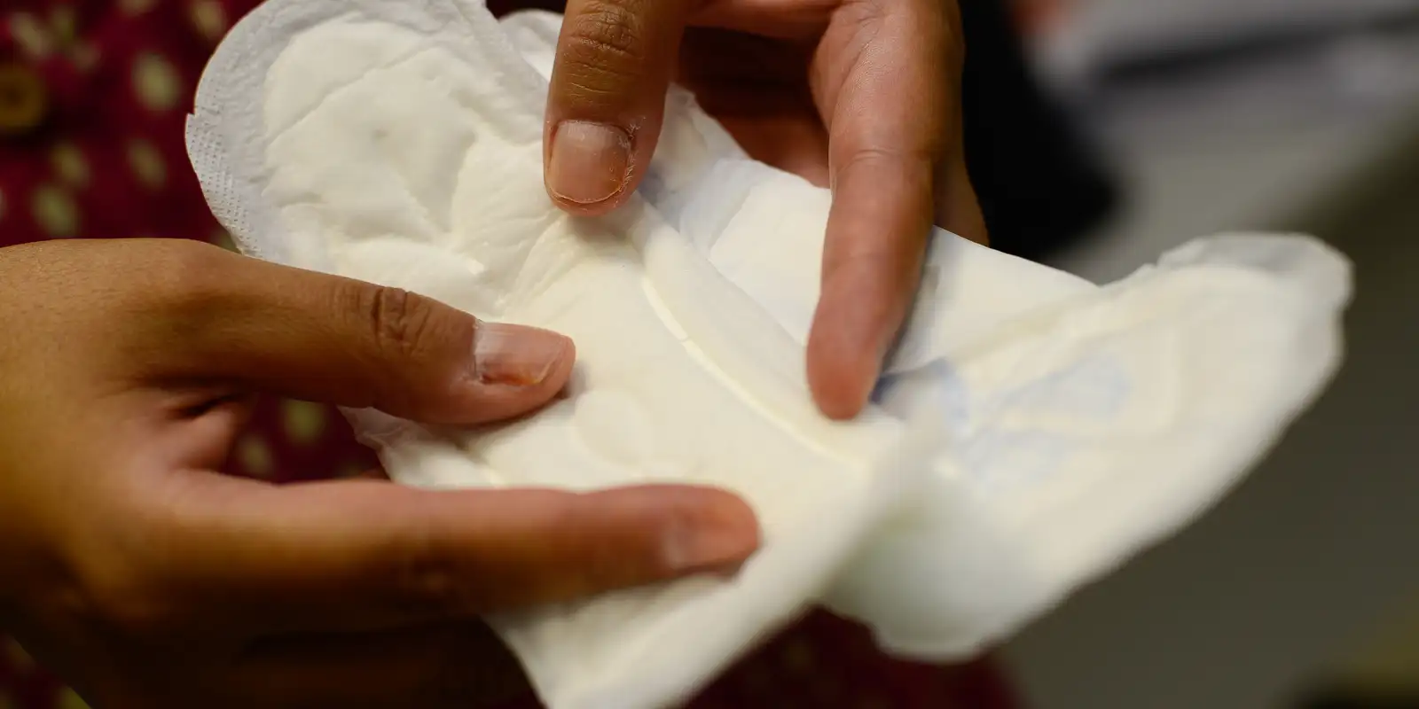 Mãos segurando um absorvente feminino branco aberto, mostrando detalhes de tecido e formato