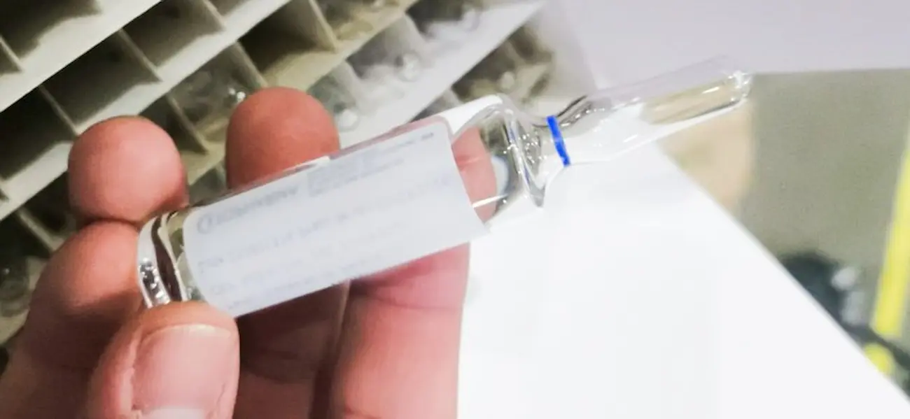 Ampola de antídoto para intoxicação por metanol sendo segurada, representando o acesso ao tratamento em diversos estados.