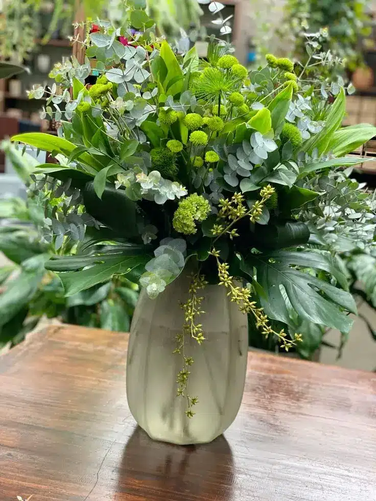 Arranjo de flores verdes com toques de amarelo e elementos naturais.