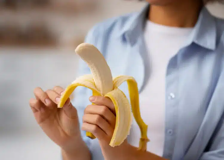 Pessoa segurando uma banana parcialmente descascada, simbolizando o momento ideal para consumir a fruta e obter seus benefícios.