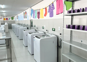 Fileira de máquinas de lavar em lavanderia pública, ilustrando o apoio do governo para reduzir a sobrecarga de trabalho feminino.